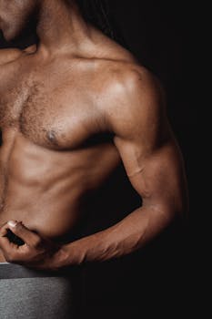 Close-up of a shirtless man flexing his bicep, showcasing muscular definition and strength.